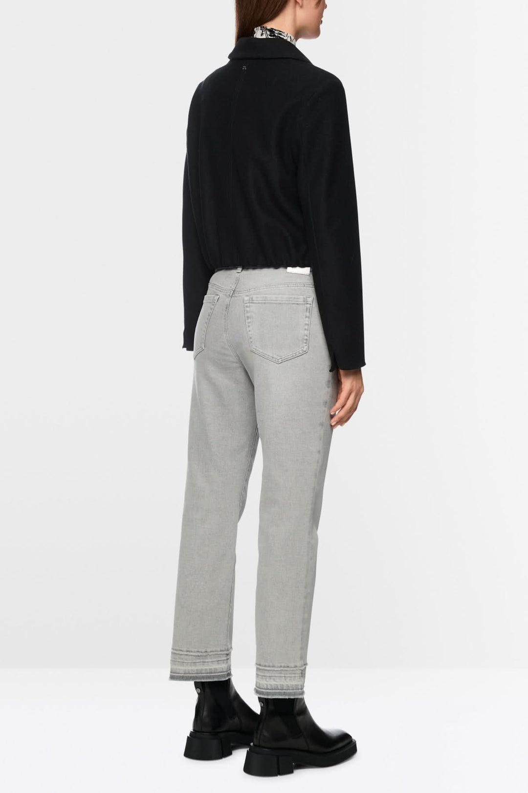 Pantalon en denim gris avec coupe droite évasée et effet effiloché, porté par une personne en veste noire et bottes noires.