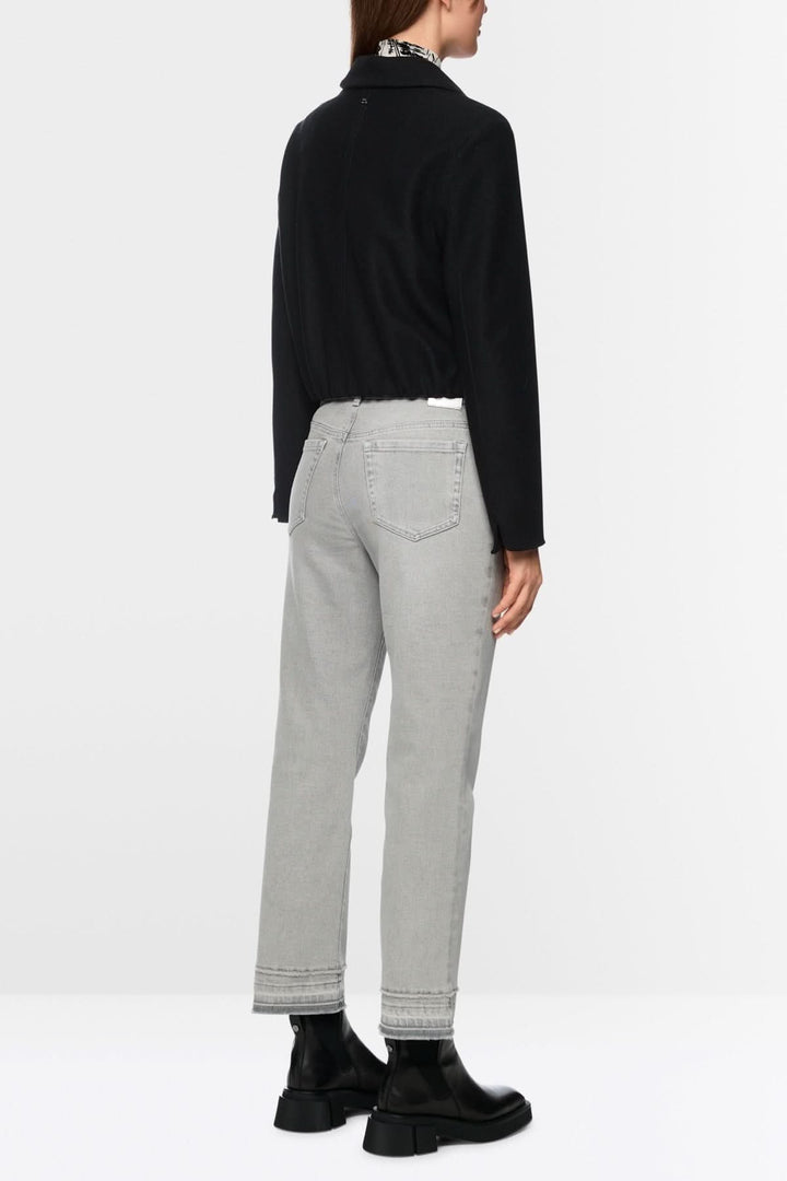 Pantalon en denim gris avec coupe droite évasée et effet effiloché, porté par une personne en veste noire et bottes noires.