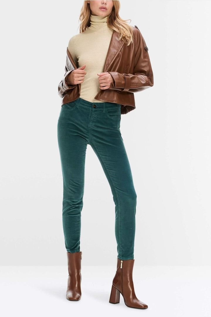 Modèle portant un pantalon en velours vert, tunique beige et veste en cuir marron, style décontracté et élégant.