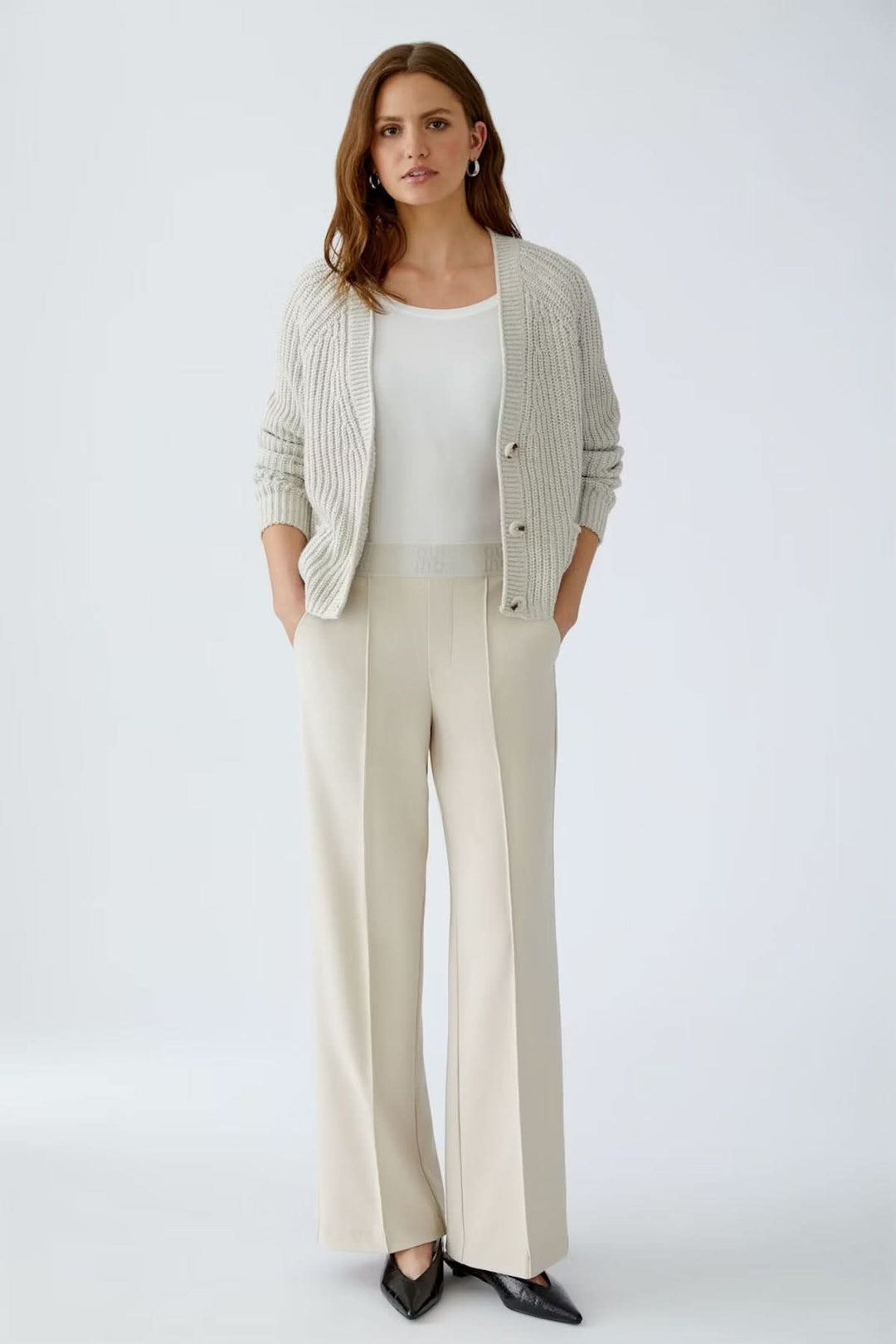 Pantalon à jambe large en jersey technique beige, porté avec un haut blanc et gilet gris, parfait pour un look élégant et confortable.