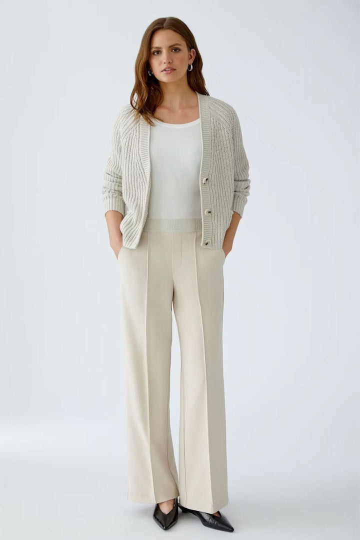 Pantalon à jambe large en jersey technique beige, porté avec un haut blanc et gilet gris, parfait pour un look élégant et confortable.