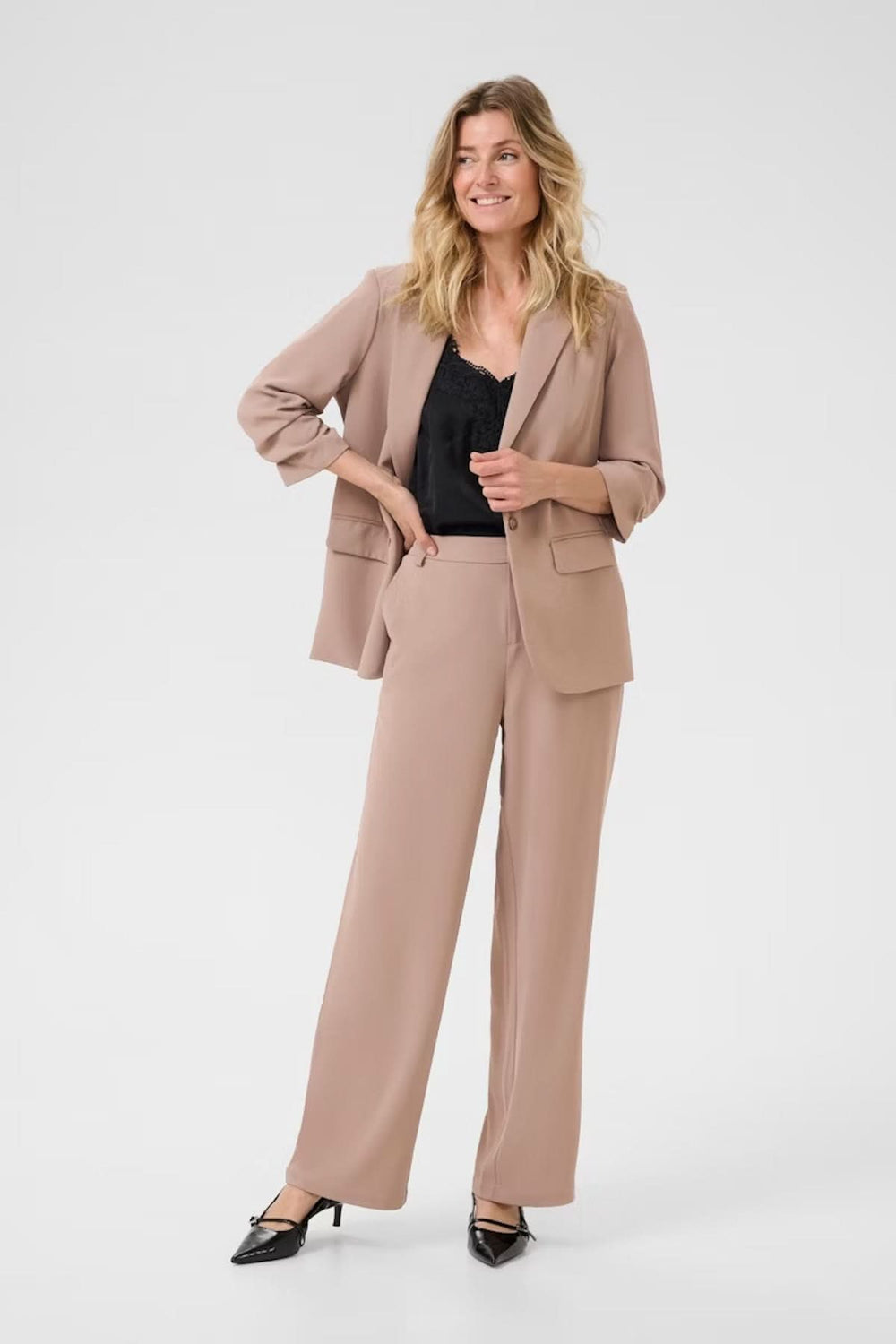 Femme souriante portant un pantalon à jambe large et un blazer, look professionnel et élégant.