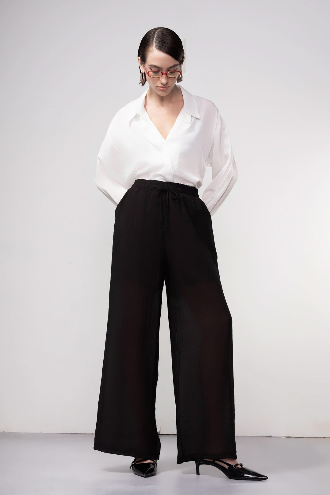 Femme portant un pantalon jambe large noir avec blouse blanche, offrant une silhouette fluide et moderne, taille élastique.