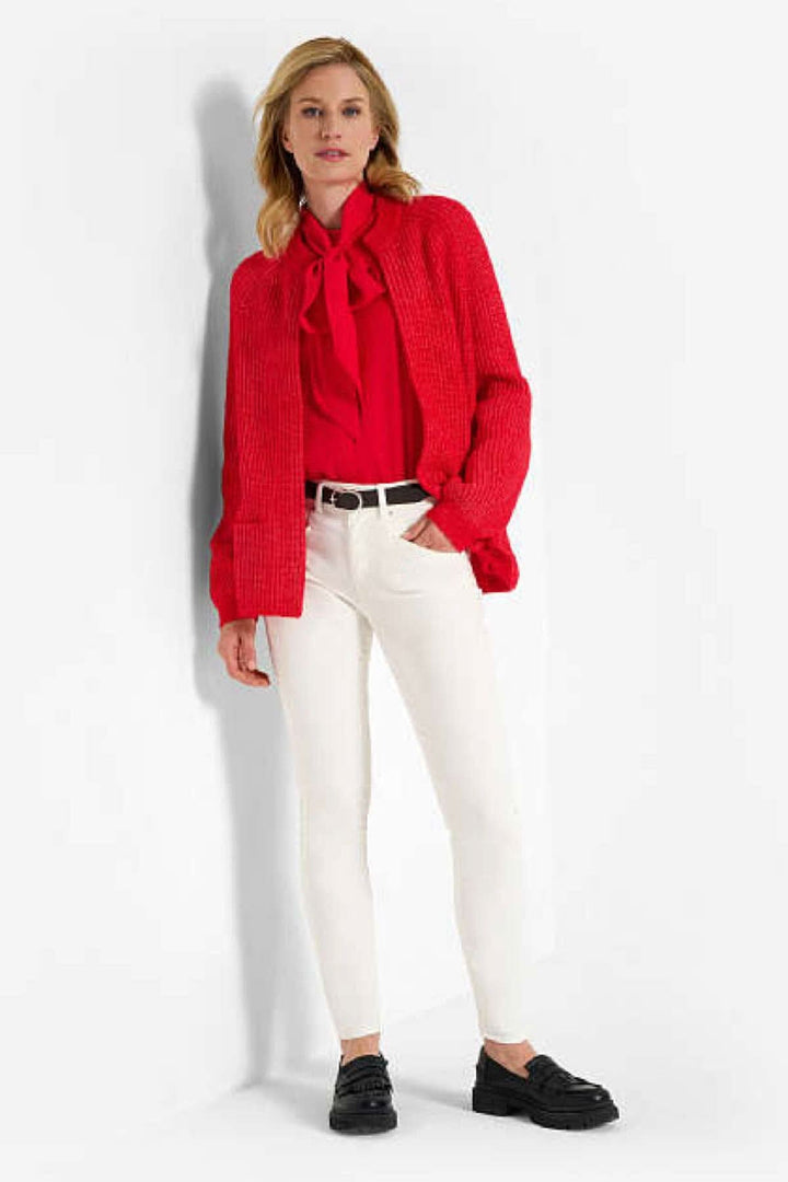 Femme en pantalon blanc et chemisier rouge avec cardigan, style décontracté et moderne.