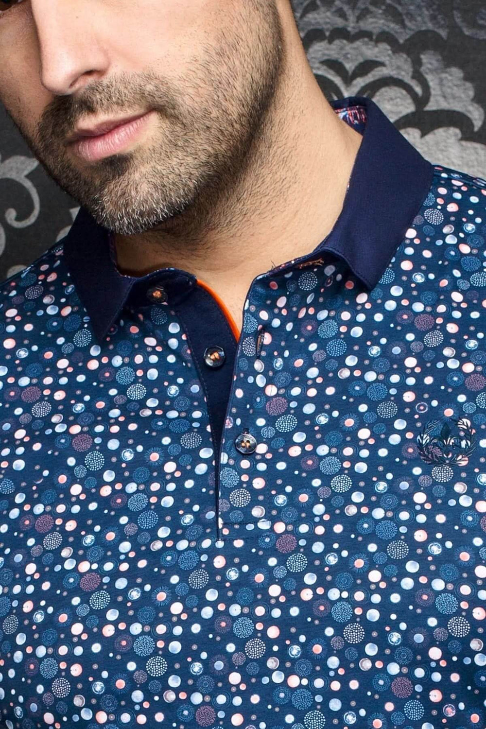 Polo Adonis à pois multicolores, col contrastant bleu marine et intérieur orange, style moderne et élégant.