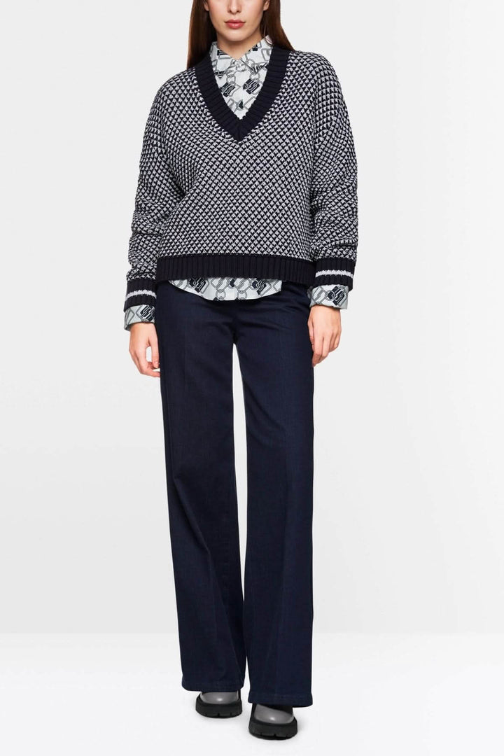 Pull court tricoté noir et blanc à encolure en V, porté avec une chemise à col et pantalon fluide.