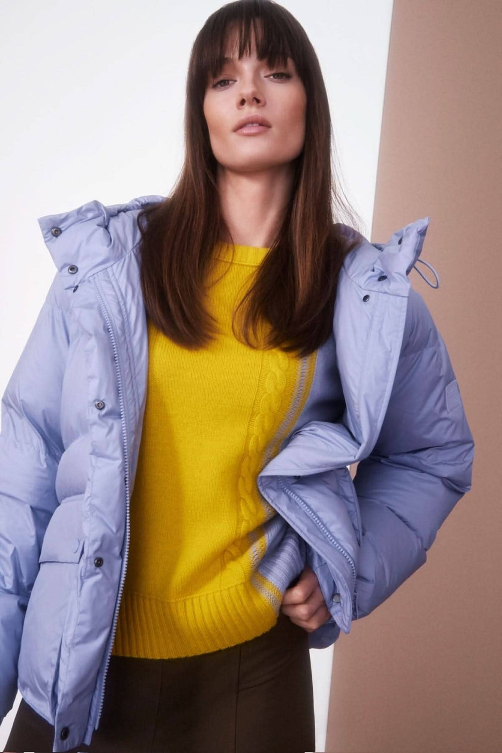 Femme portant un pull tricoté jaune et une doudoune bleue, affichant un look élégant et moderne.