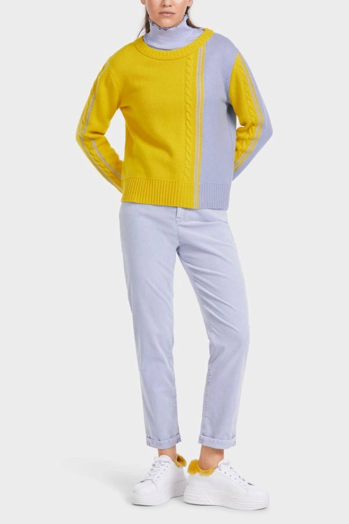Pull tricoté bicolore jaune et lavande avec encolure ronde, porté avec un pantalon clair et des sneakers blanches.