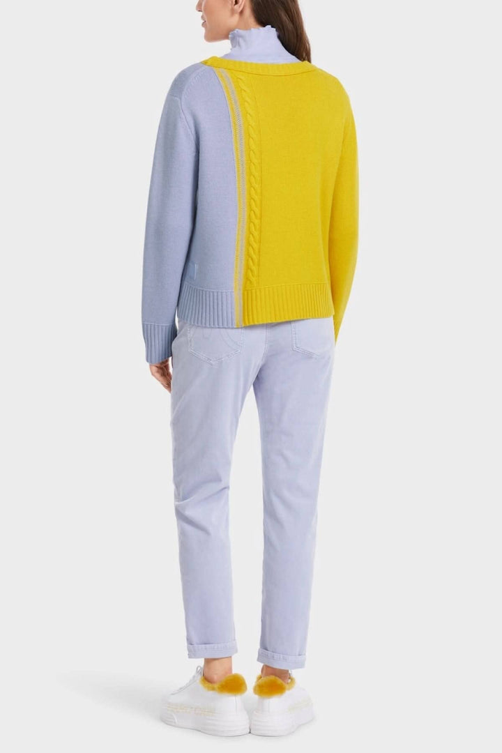 Pull tricoté bicolore en laine, avec motifs asymétriques, porté avec un pantalon clair.