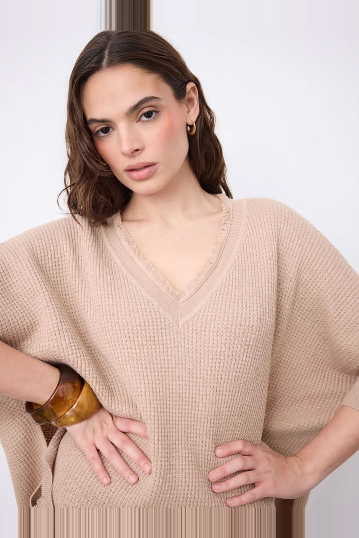 Femme portant un pull poncho col V à manches ¾ en coton cachemire gaufré, avec finitions frangées et fentes latérales, pose de mode.