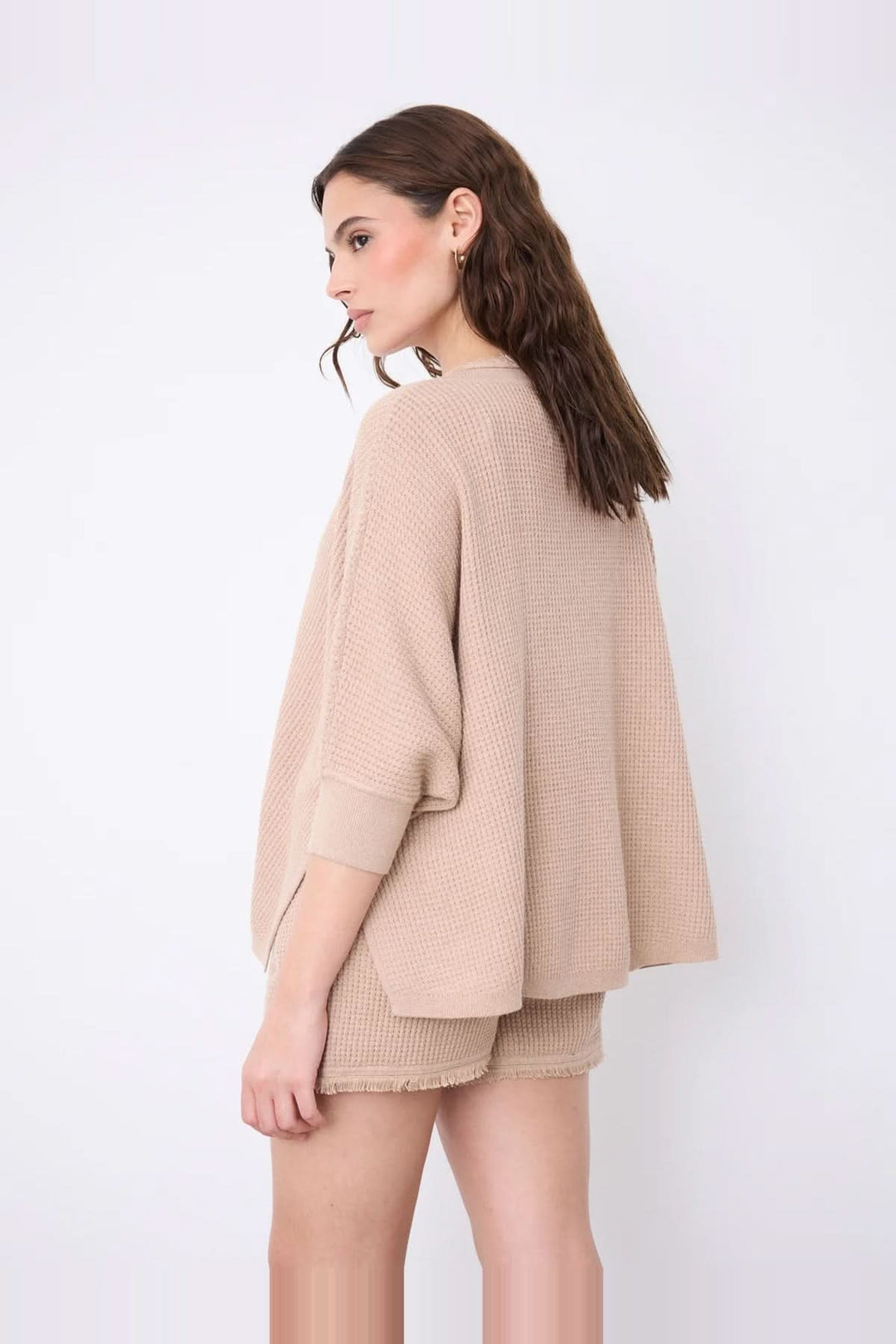 Femme portant un pull poncho col V à manches ¾ en coton cachemire, couleur beige, avec finitions frangées.