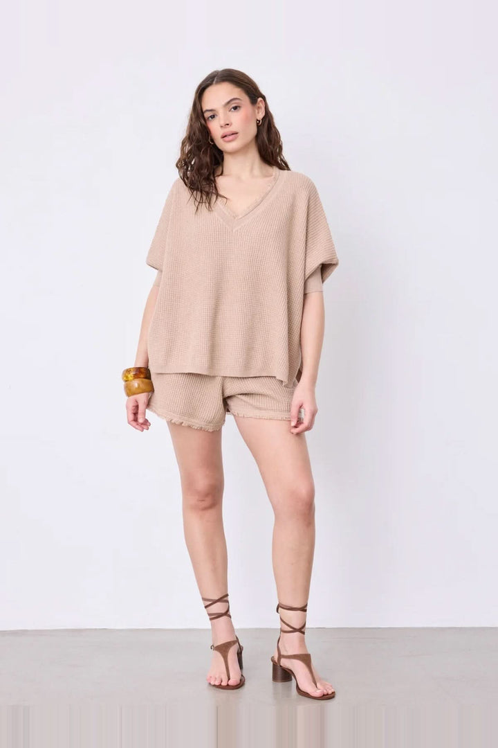 Femme portant un pull poncho col V à manches ¾ en coton cachemire avec finitions frangées et texture douce, couleur beige.
