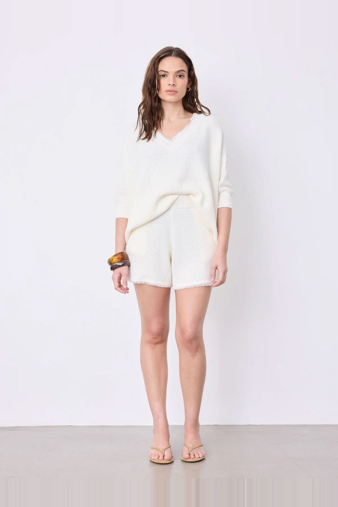 Femme portant un pull poncho col V à manches ¾ en coton cachemire avec finitions frangées, style moderne et fluide.