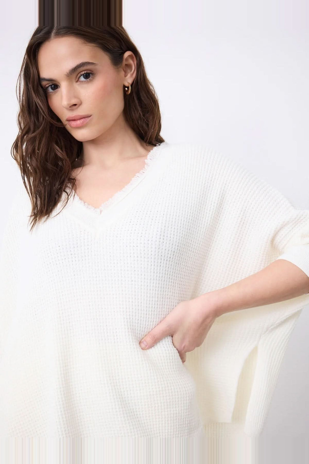 Femme portant un pull poncho col V à manches ¾ en coton cachemire gaufré avec finitions frangées et fentes latérales.