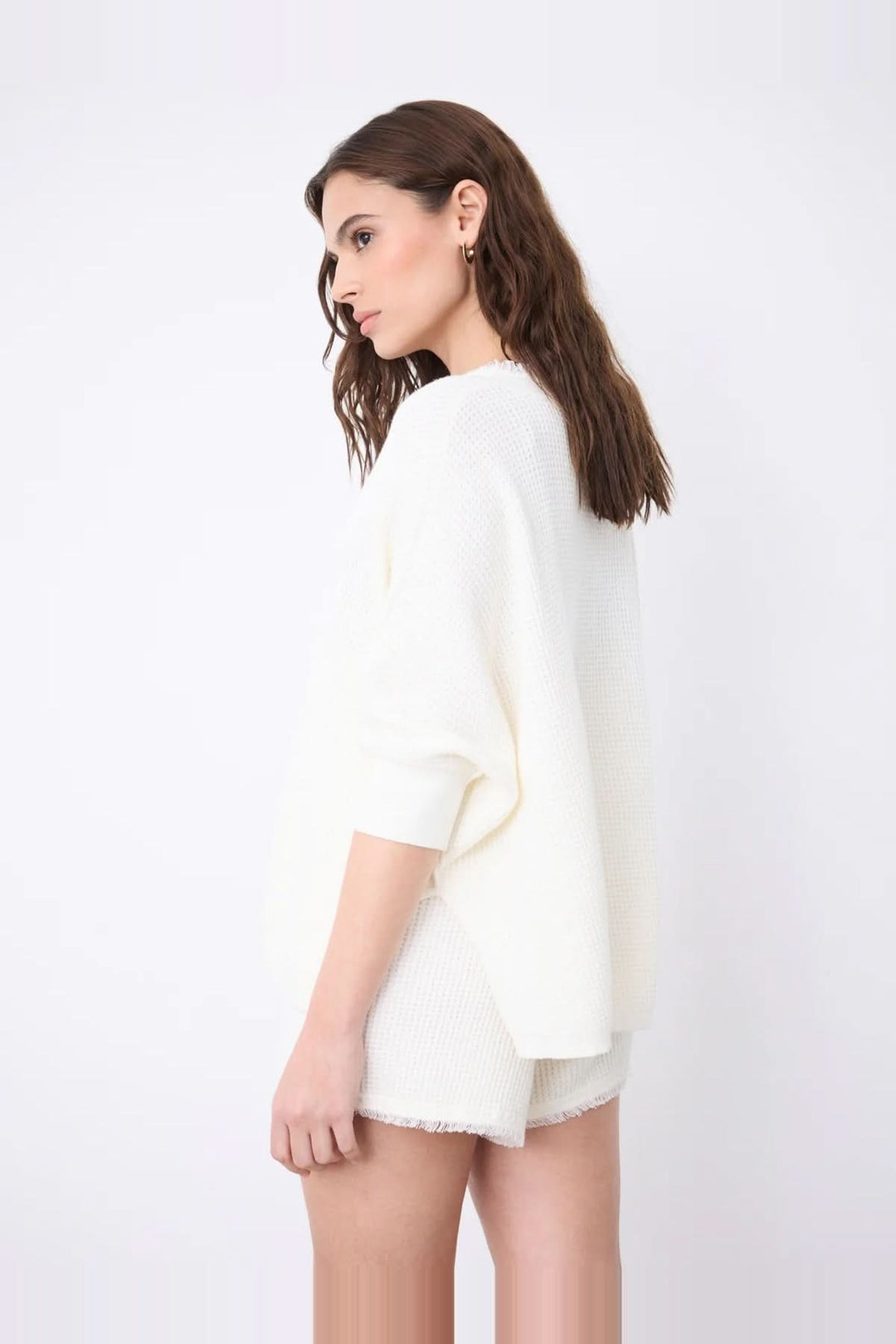 Pull poncho col V à manches ¾ en coton cachemire blanc avec finitions franges, porté par un modèle de profil.