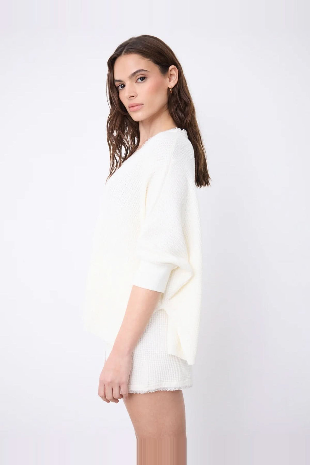 Femme portant un pull poncho col V à manches ¾ en coton cachemire blanc, vue de côté, avec finitions franges et fentes latérales.