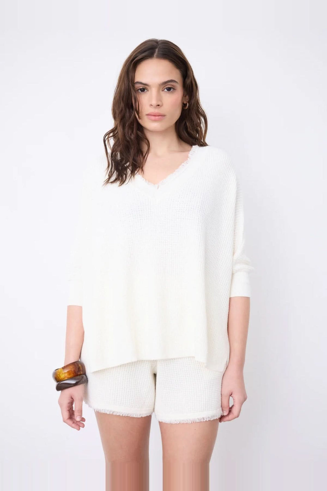 Pull poncho col V à manches ¾ en coton cachemire blanc avec finitions frangées, silhouette fluide pour un style moderne et confortable.