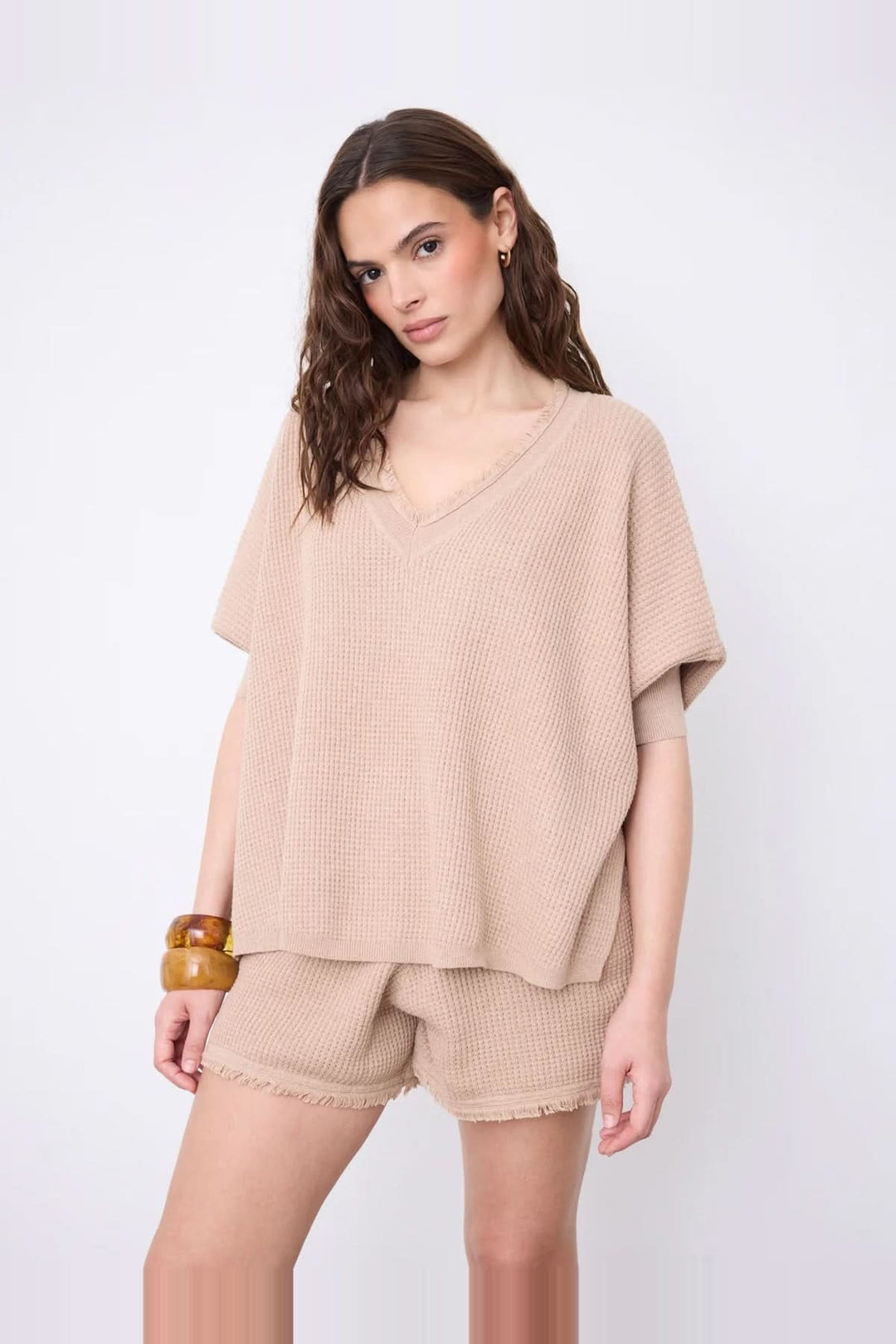 Model wearing Pull poncho col V à manches ¾ in beige cotton cashmere with fringed edges and side slits for a modern look.
