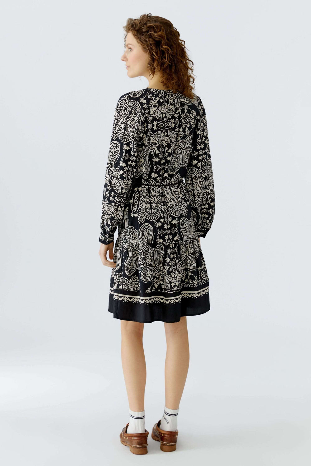 Femme portant une robe courte imprimé graphique avec ceinture à nouer, inspirée du style bohème, vue de dos, coupe droite légèrement évasée.