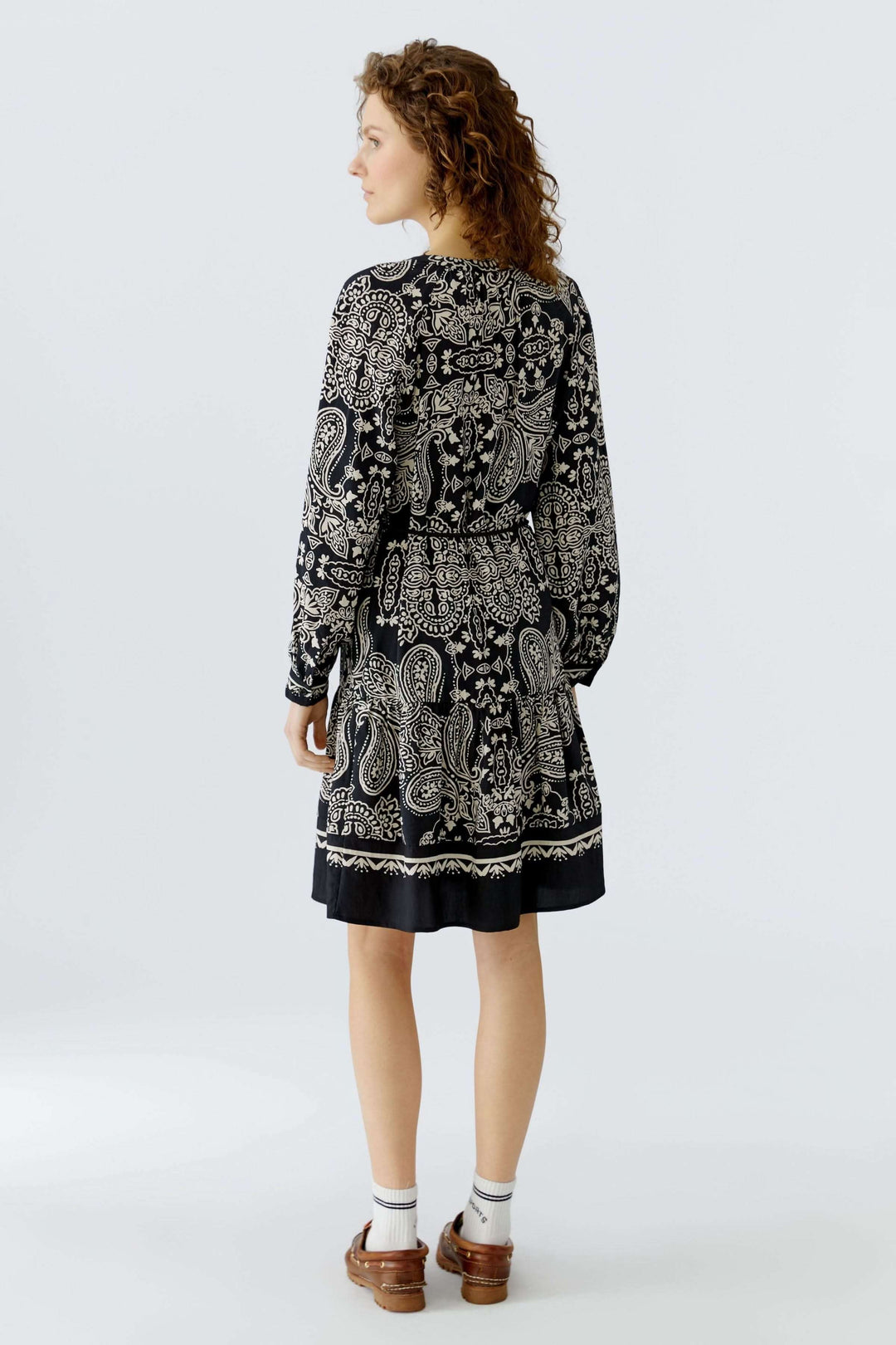 Femme portant une robe courte imprimé graphique avec ceinture à nouer, inspirée du style bohème, vue de dos, coupe droite légèrement évasée.
