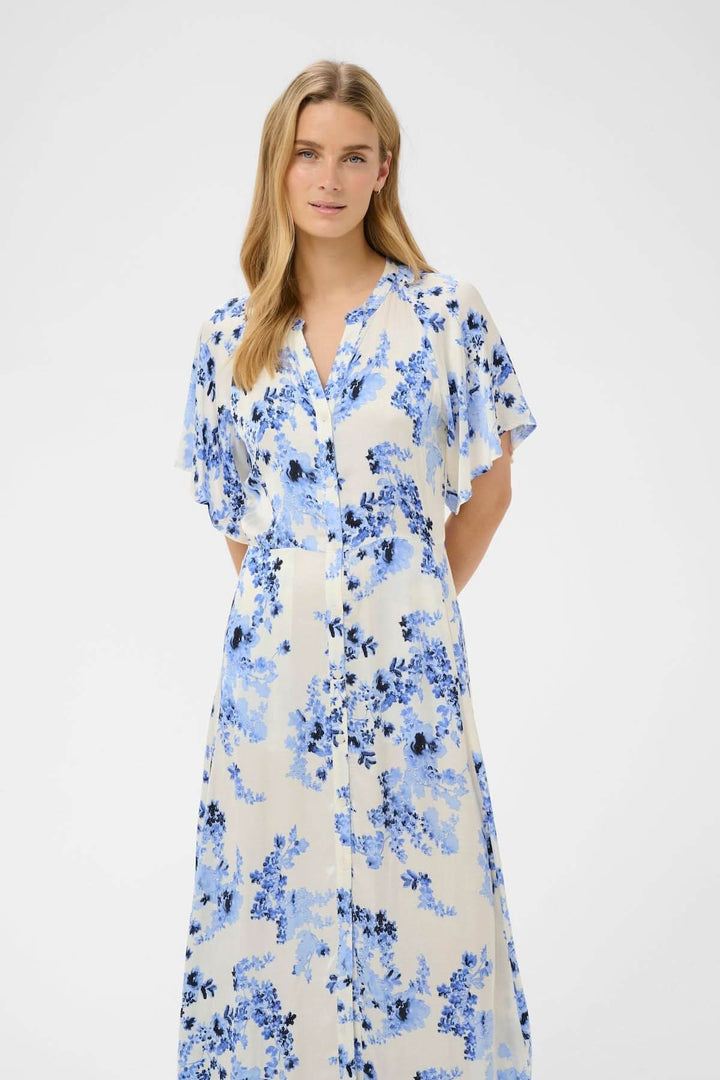 Femme portant Robe fleurie Alaja, une robe midi fluide à imprimé floral bleu, coupe droite élégante et raffinée avec boutonnage classique.