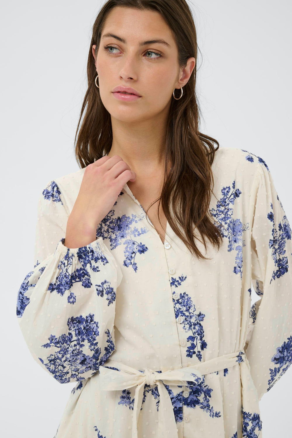Femme portant une Robe fleurie Avira avec motif floral délicat et ceinture à nouer, manches longues bouffantes.