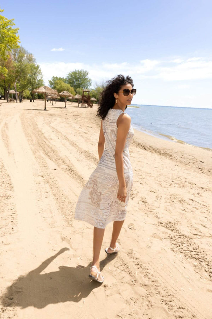 Femme en robe imprimée sans manches marchant sur la plage, montrant une coupe fluide et un style estival idéal pour les escapades ensoleillées.