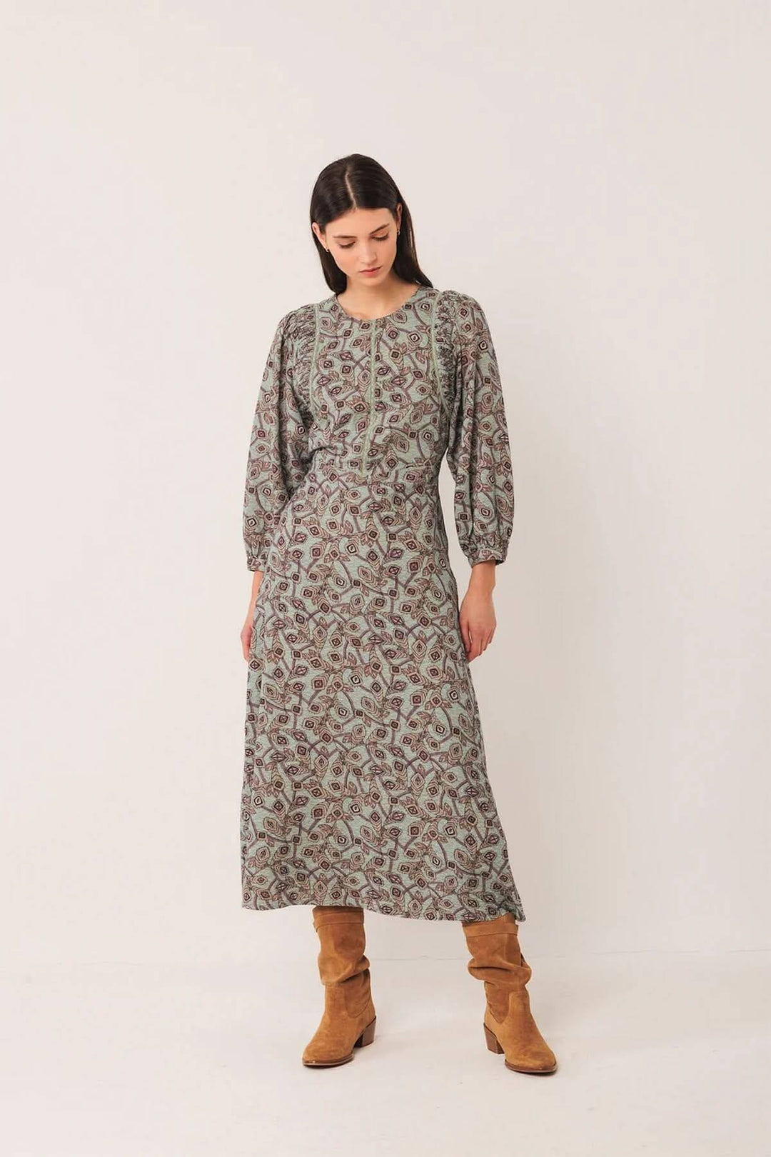 Robe longue au motif géométrique avec manches longues bouffantes et encolure ronde, portée avec des bottes en daim pour un style bohème chic.