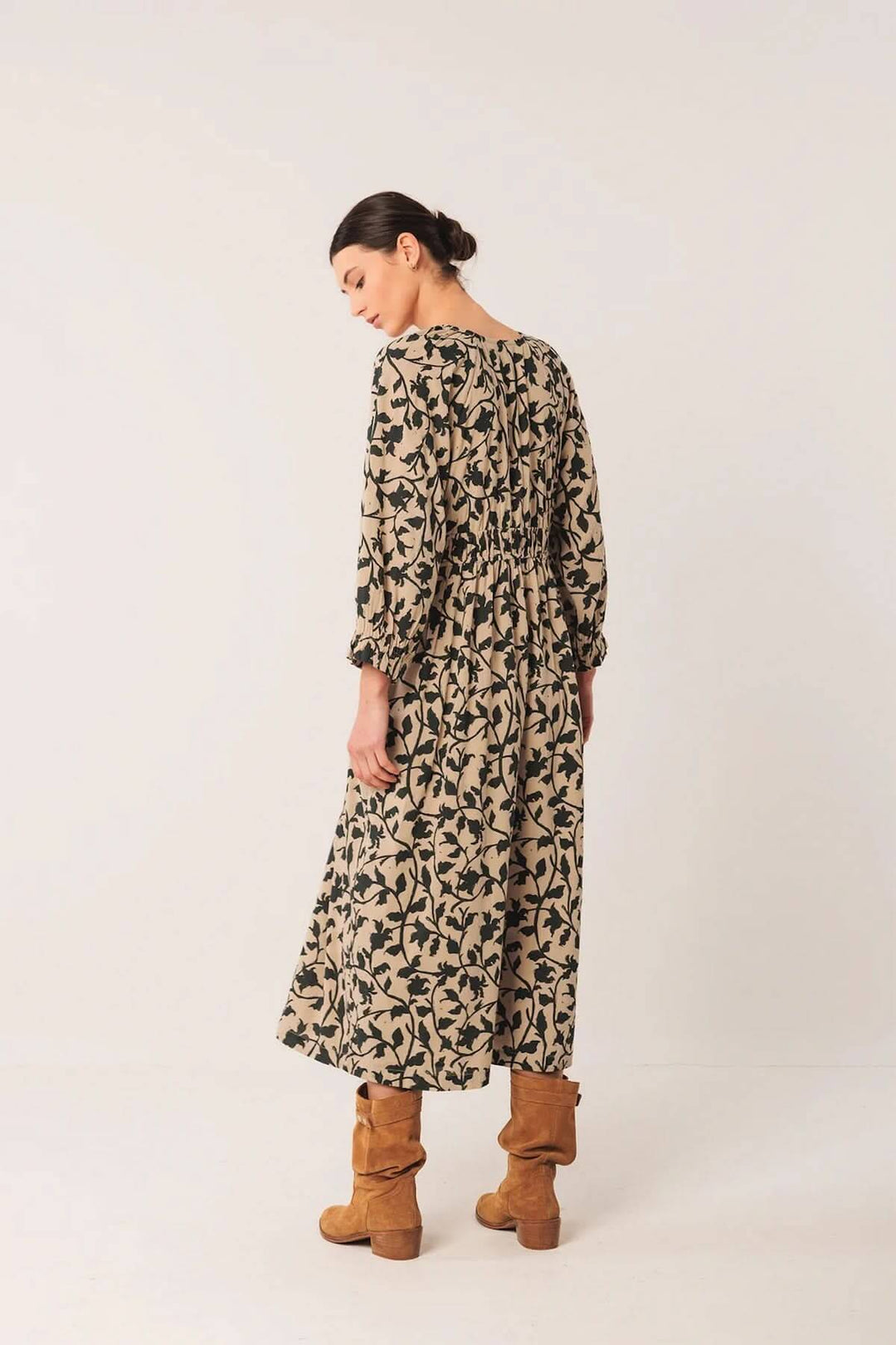 Femme portant une robe longue fluide avec imprimé botanique, vue de dos, associée à des bottes en cuir pour un look bohème.
