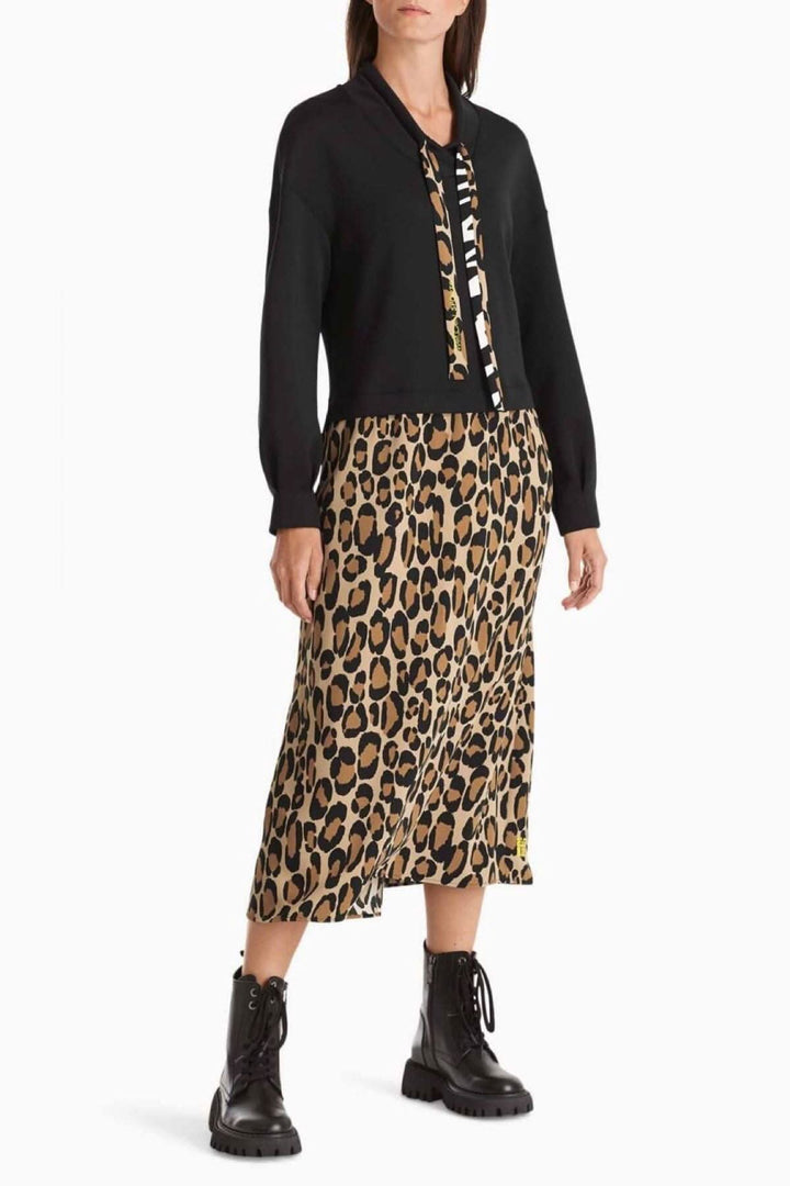 Femme portant une robe longue imprimé léopard avec un cardigan noir et des bottes noires, style décontracté.