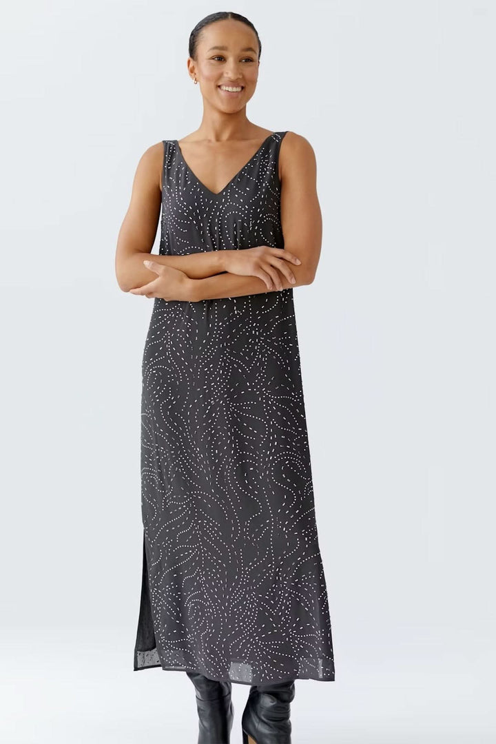 Femme portant une robe longue sans manches avec imprimé pointillé et encolure en V, stylisée avec des bottes hautes noires.