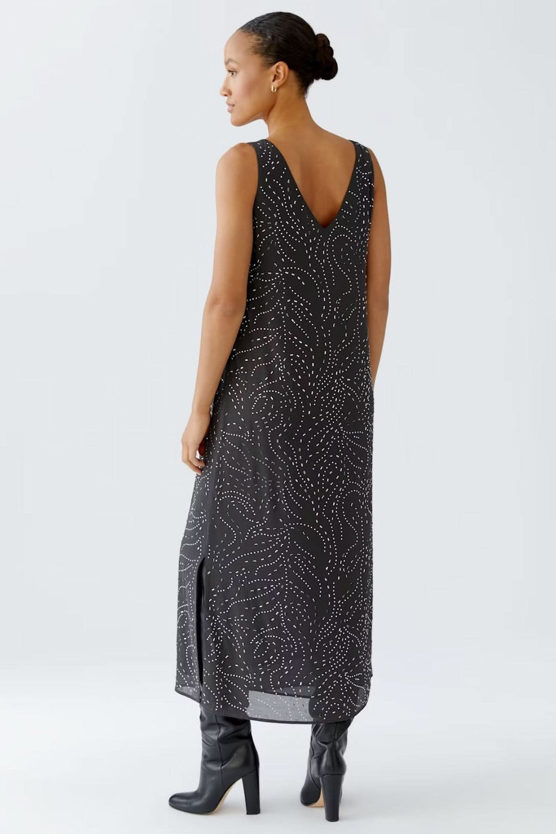 Robe longue sans manches avec imprimé discret en pointillés, encolure en V, fentes latérales, portée avec des bottes hautes.