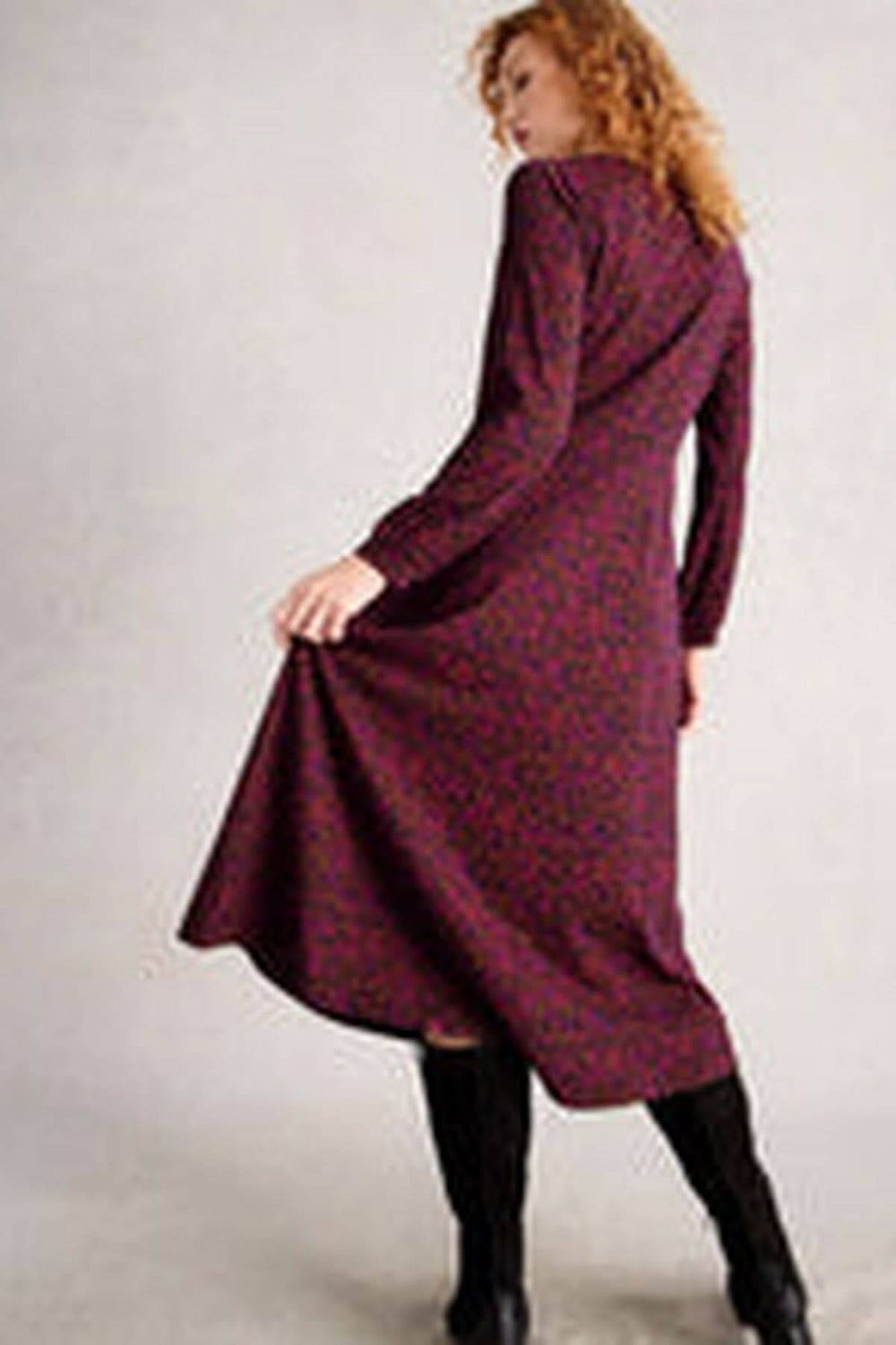 Femme portant une robe midi en jersey col en V avec manches longues et jupe évasée, associée à des bottes hautes noires.