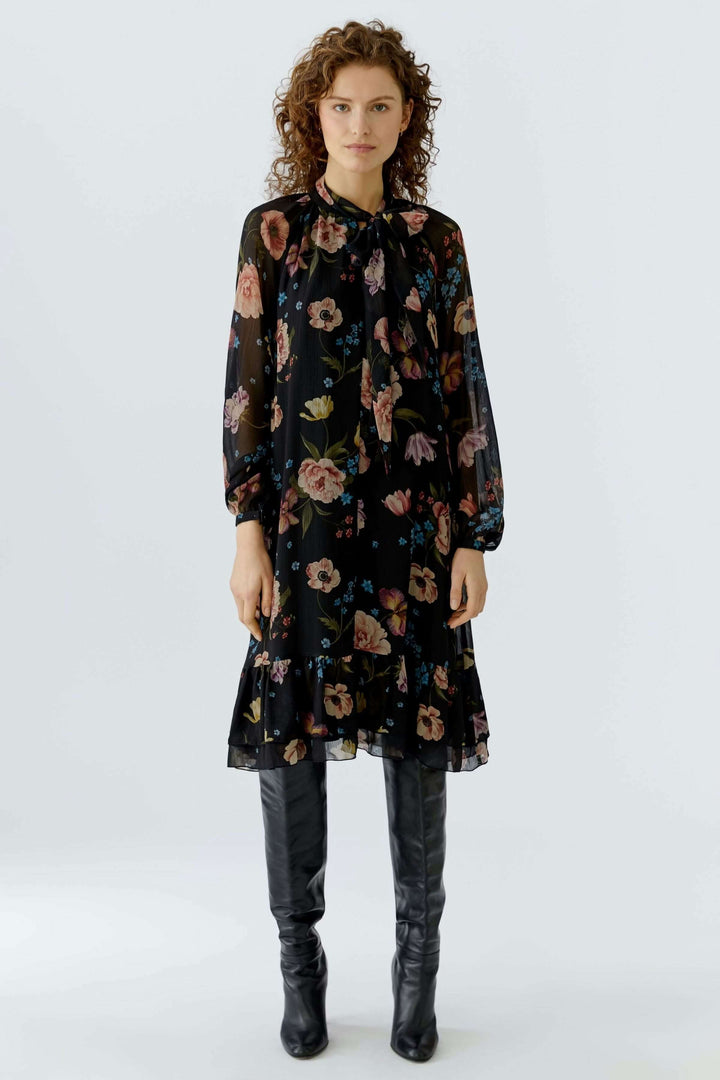 Robe midi fluide avec imprimé floral et lien à nouer, portée avec bottes noires, style féminin et élégant pour la saison.