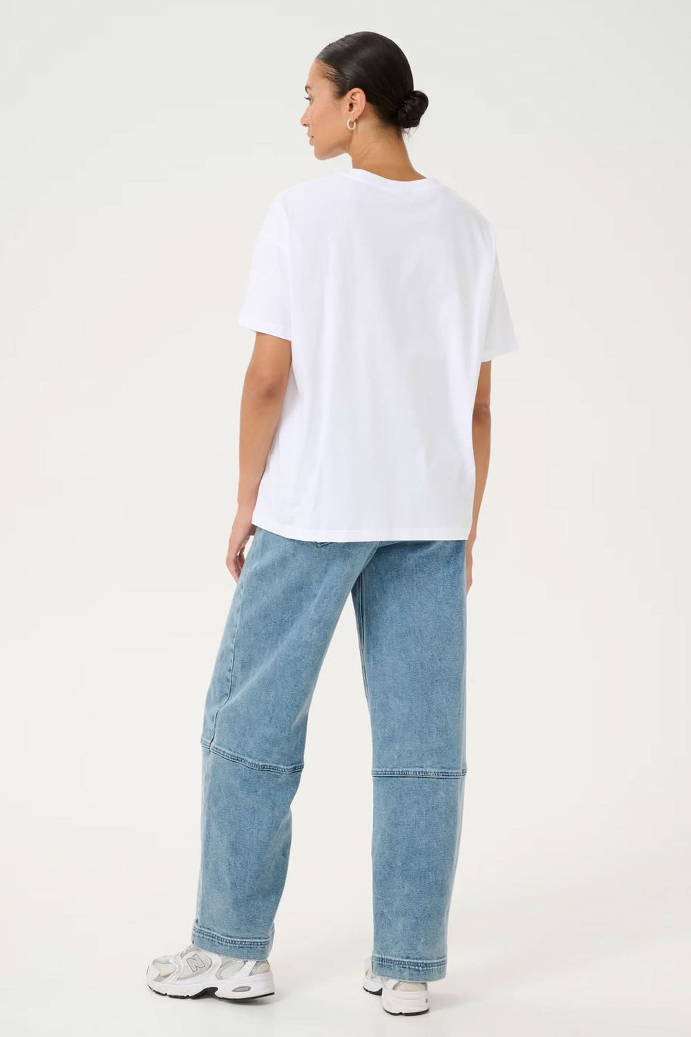 Modèle de dos portant un T-shirt blanc décontracté, associé à un jean ample, pour un look moderne et stylé.