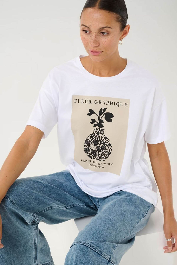 T-shirt blanc avec imprimé floral graphique, encolure ronde, coupe décontractée, porté avec un jean.
