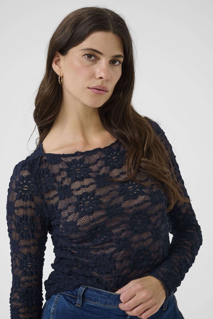 Femme portant le T-shirt Maddie, en dentelle noire avec manches longues et coupe ajustée pour un look sophistiqué et féminin.