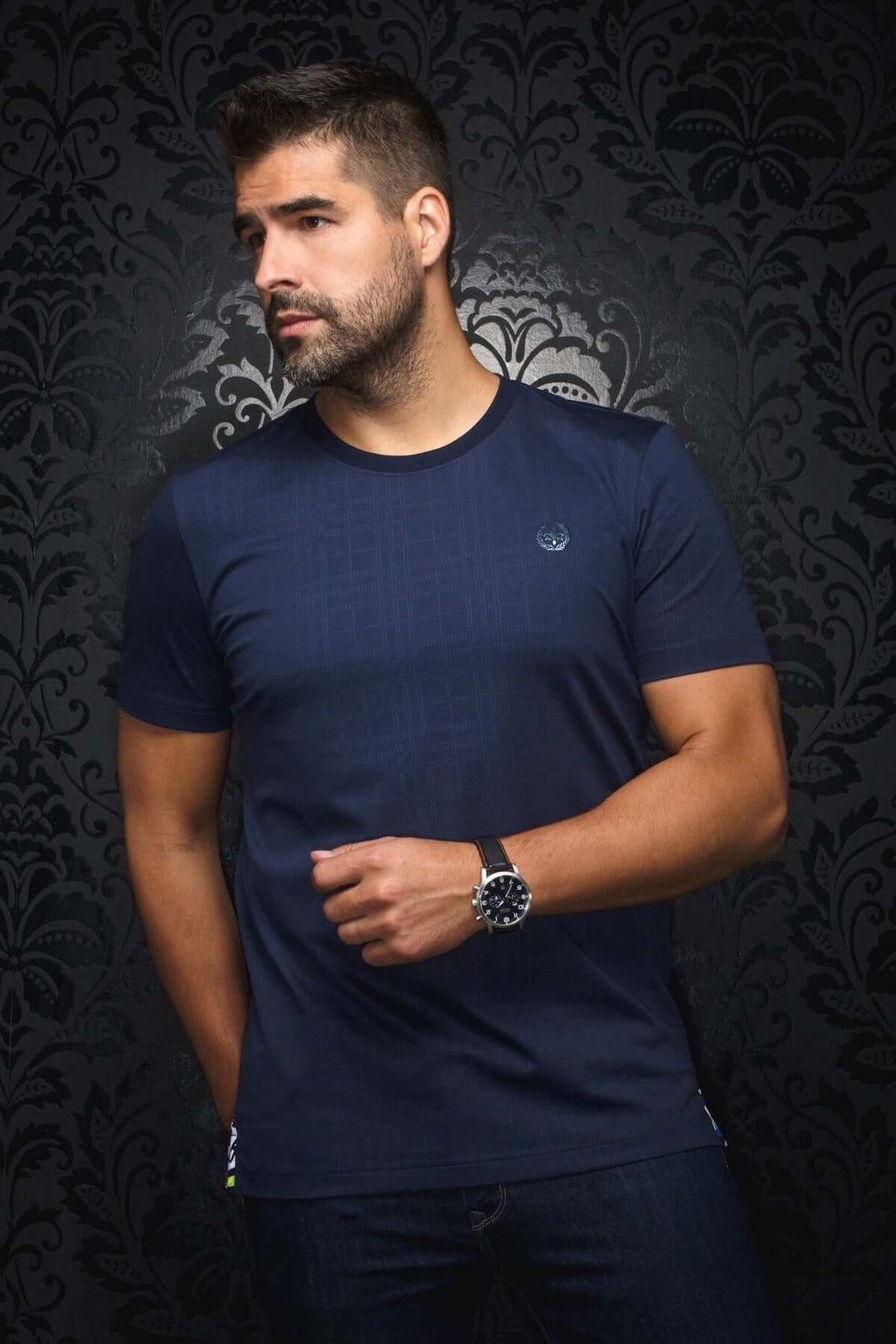 Homme portant un t-shirt Varenna bleu navy avec un motif ton sur ton et logo brodé, pose urbaine élégante.
