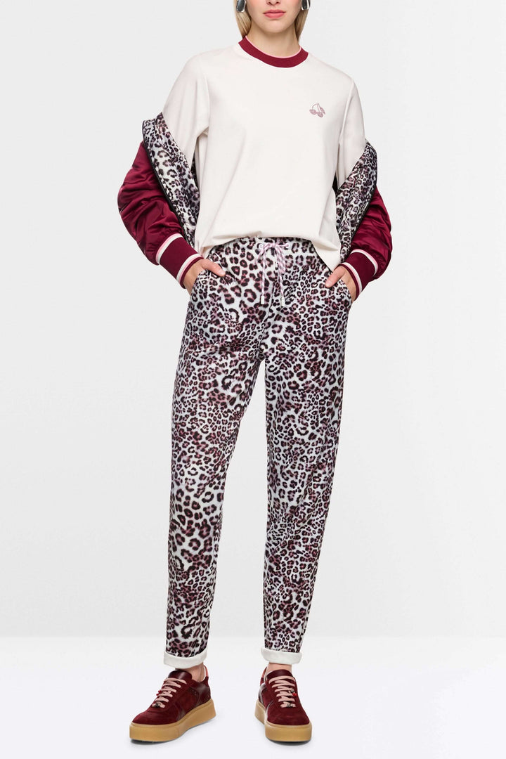 Femme portant un T-shirt classique avec manches longues et col contrasté, logo Marc Cain Sport, tenue décontractée avec pantalon imprimé léopard.