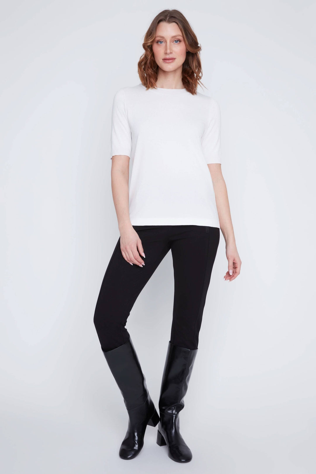 Femme portant un t-shirt classique blanc à manches courtes avec un pantalon noir et bottes, style minimaliste et élégant