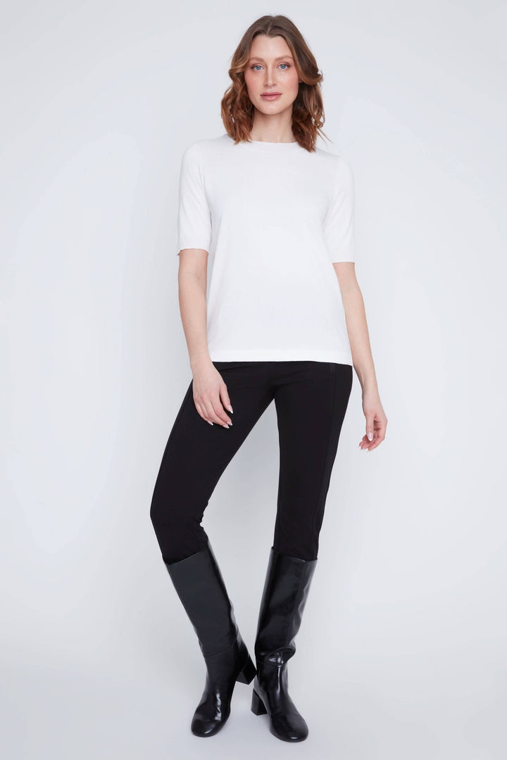Femme portant un t-shirt classique blanc à manches courtes avec un pantalon noir et bottes, style minimaliste et élégant
