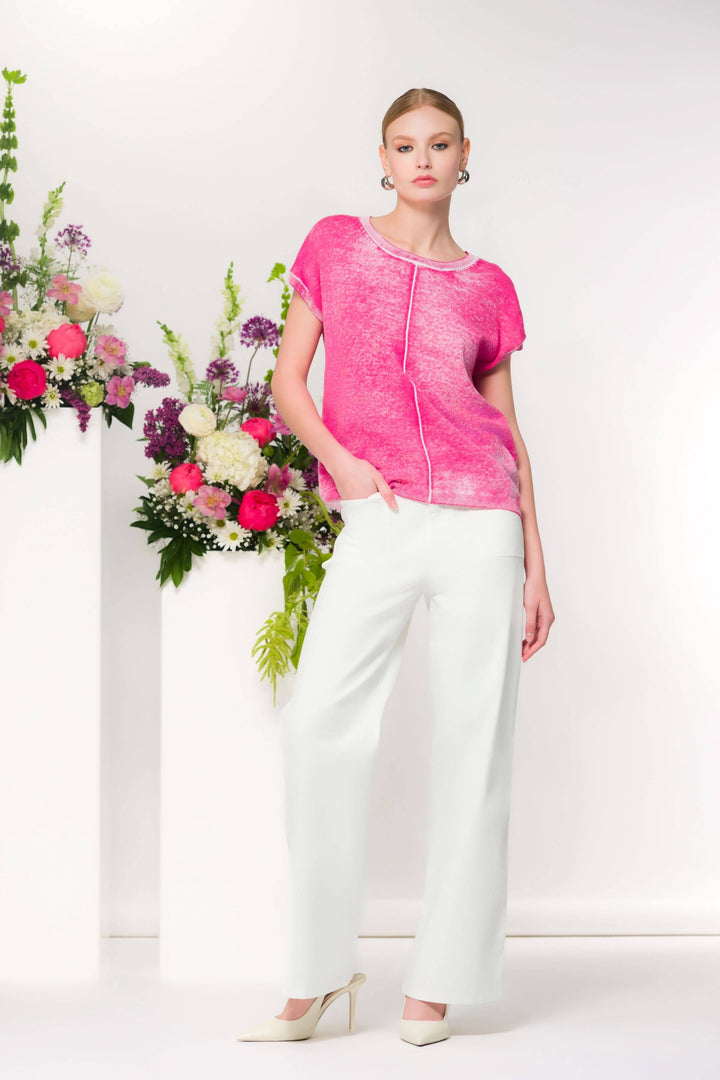 T-shirt fluide rose à maille légère porté par un mannequin devant des fleurs, coupe droite avec coutures apparentes, style décontracté.