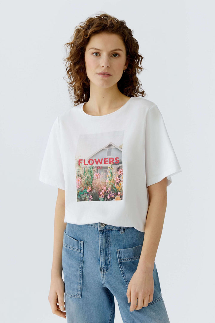 Femme portant un T-shirt imprimé graphique "Flowers" style décontracté, coupe droite, manches courtes. Facile pour un look moderne.