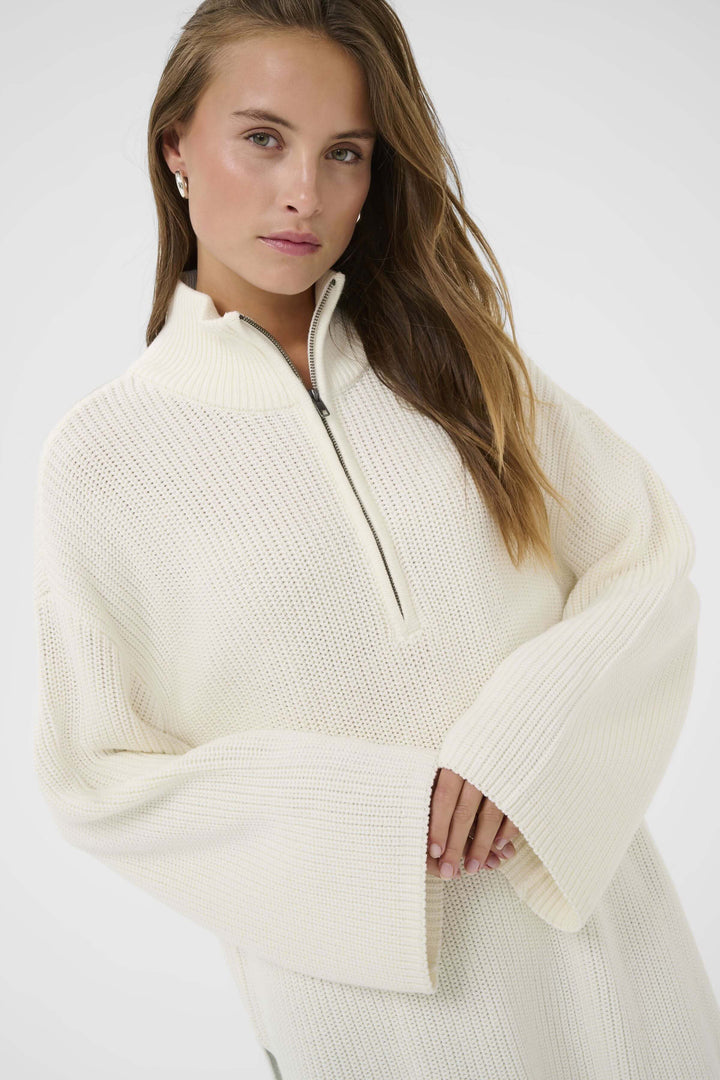 Femme portant le Tricot Pietra avec col montant zippé, offrant une coupe ample et allongée pour un style décontracté et moderne.