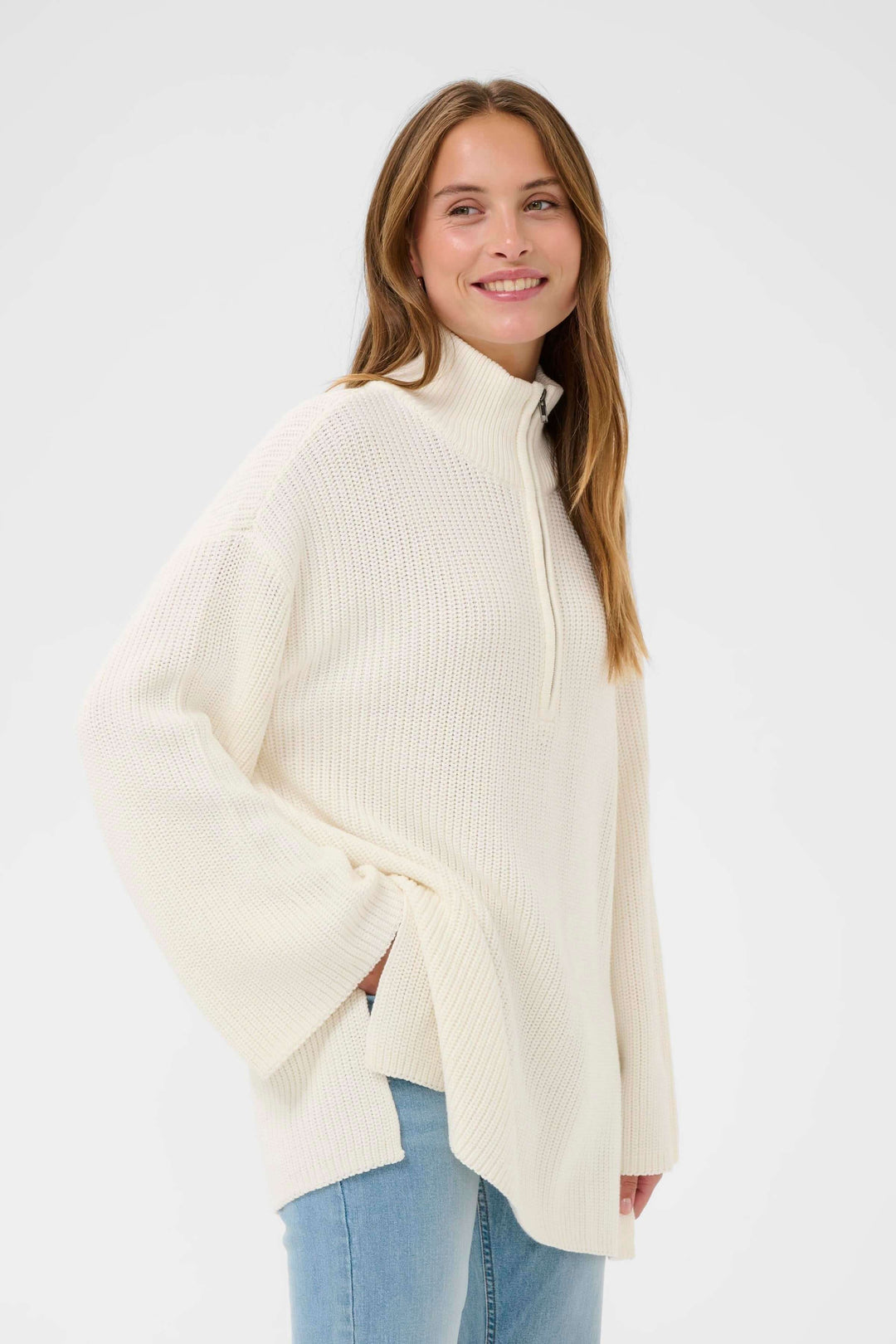 "Tricot Pietra" - pull ample en maille beige avec col montant zippé pour une allure décontractée et chaleureuse, sur fond blanc.