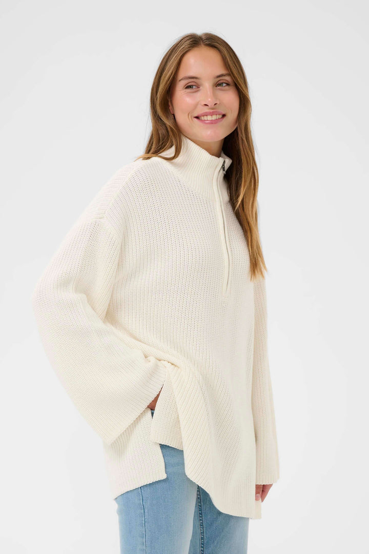 "Tricot Pietra" - pull ample en maille beige avec col montant zippé pour une allure décontractée et chaleureuse, sur fond blanc.