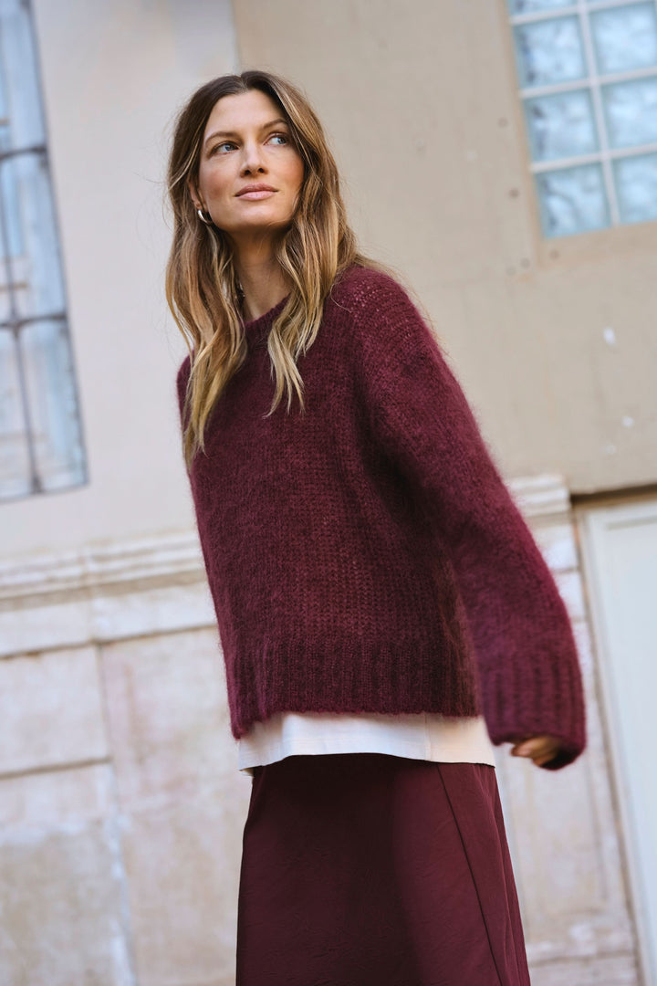 Tricot Sile à col rond, ample et confortable, porté avec une jupe dans un cadre élégant.