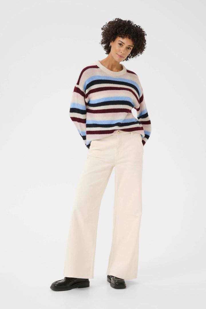 Femme portant un Tricot Spence rayé multicolore avec un jean blanc, look décontracté chic et confortable.