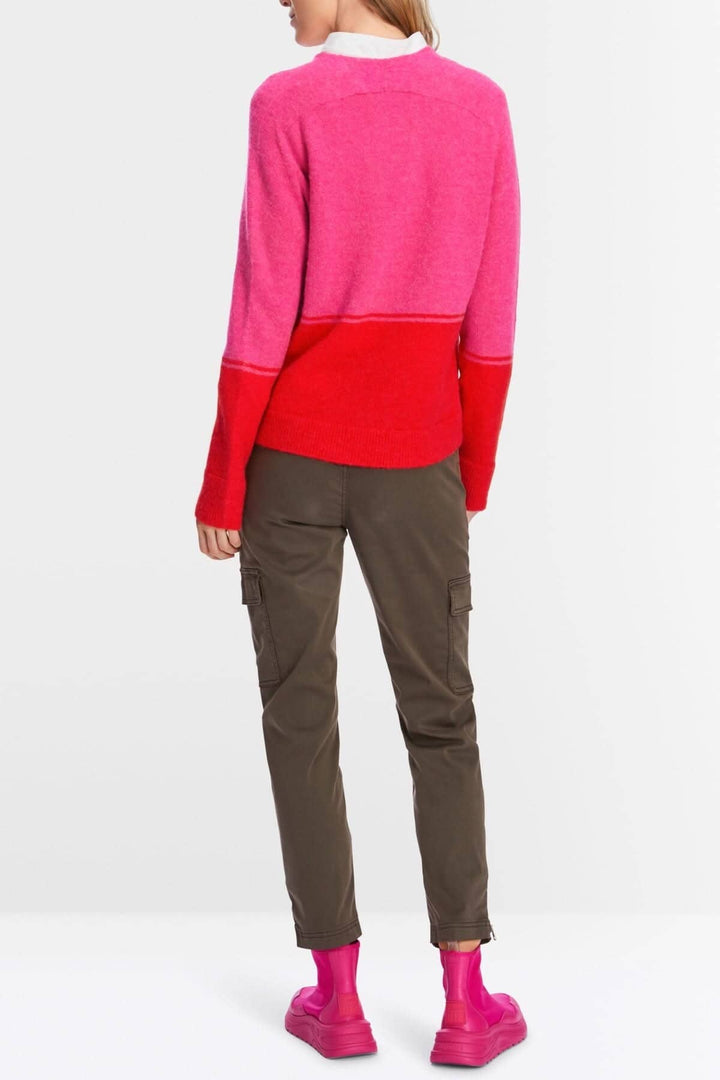 Tricot bicolore en rose et rouge, à encolure en V, porté avec un pantalon cargo et des bottes roses.