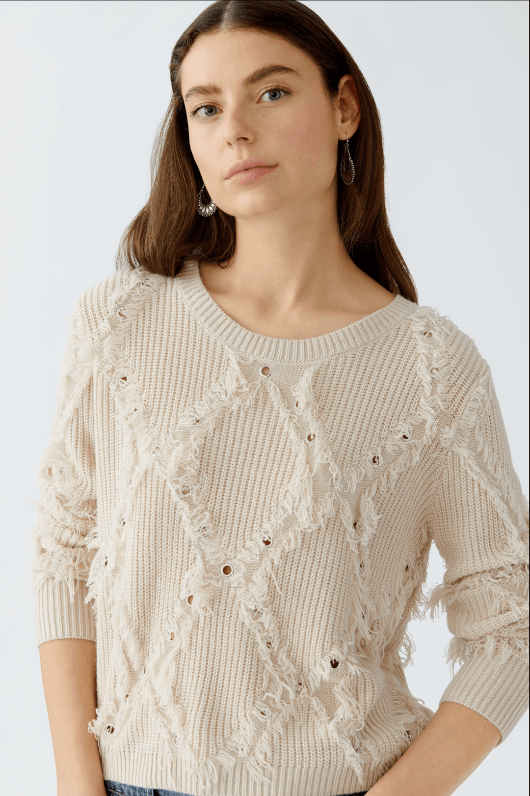 Tricot motif losange avec franges et détails métalliques, coupe décontractée, col ras du cou, porté par une femme, style contemporain.